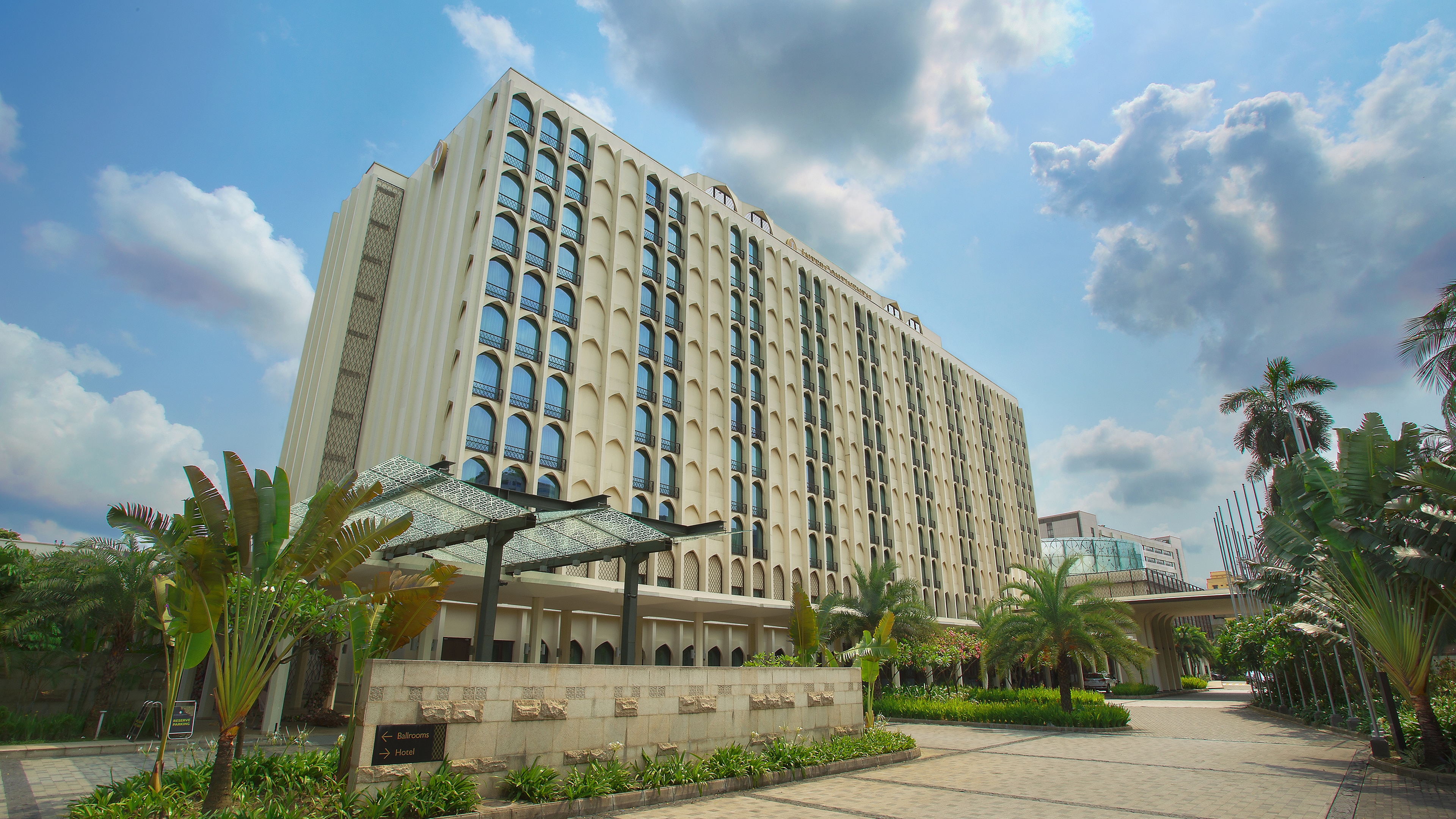 Exterior daytime view of InterContinental Dhaka with arched windows, landscaped driveway and palm trees